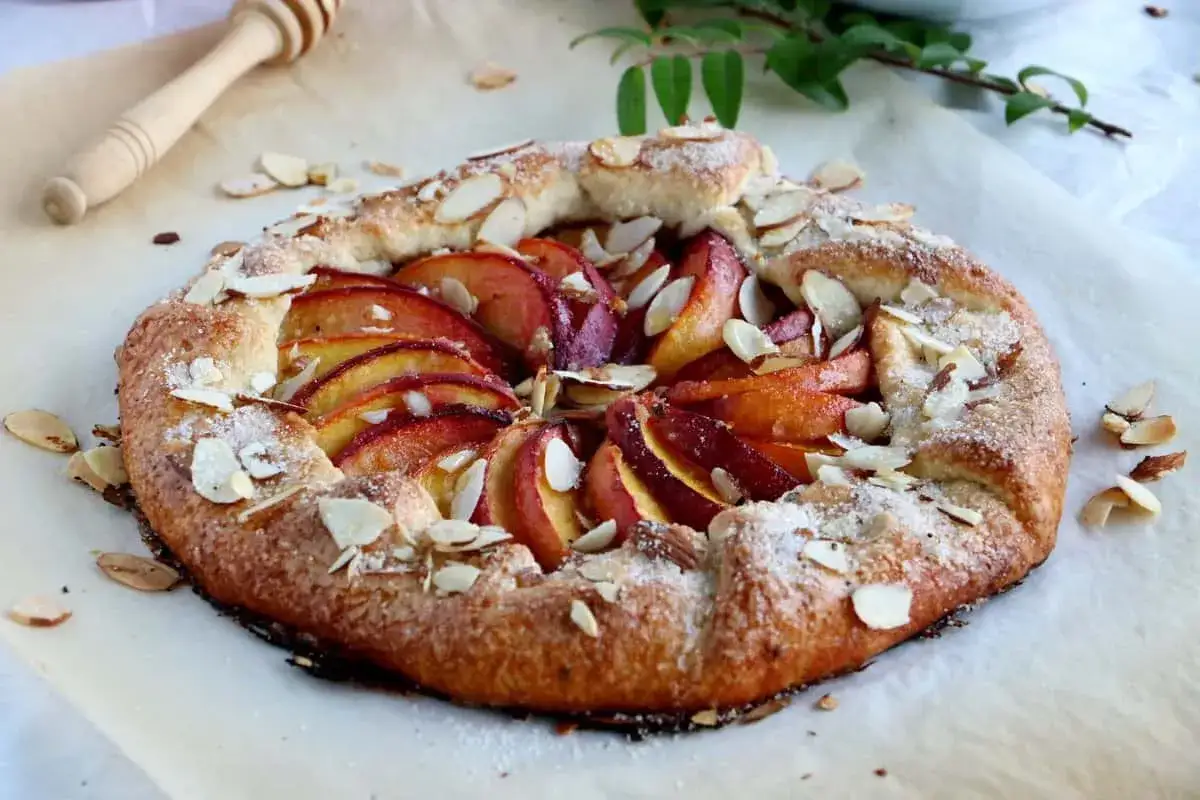 Délicieuse tarte aux pêches amande, garnie de fruits juteux et d'amandes effilées, prête à être dégustée.