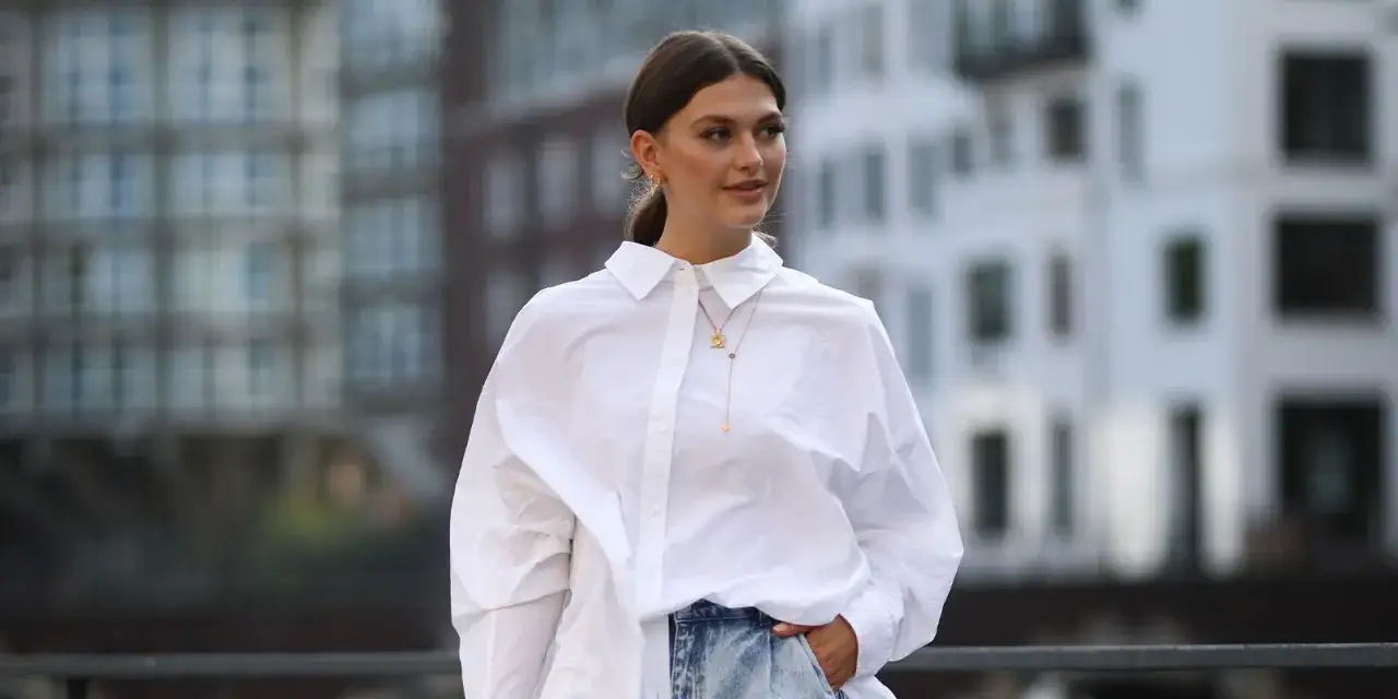 Une femme porte une chemise oversize blanche avec un jean. Elle montre comment porter une chemise oversize avec style.