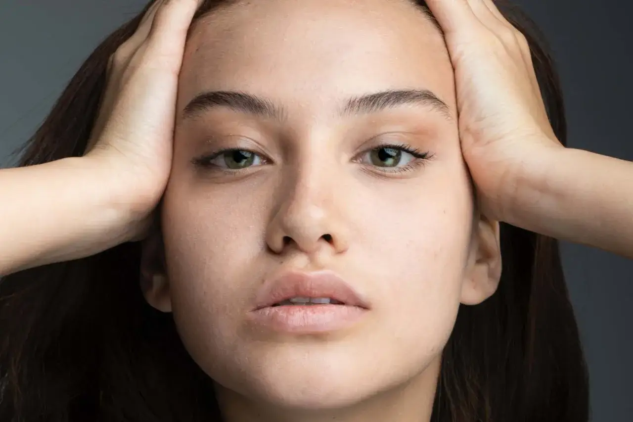 Primo piano di una giovane donna con mani tra i capelli, che evidenzia l'elasticit&agrave; della pelle e uno sguardo intenso.