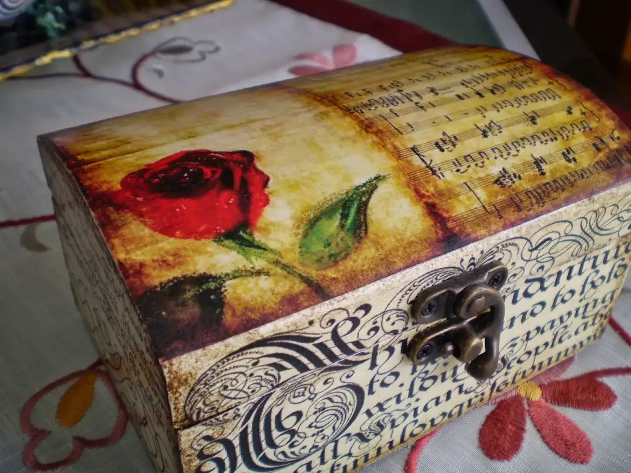 Caja decorada con rosa y partitura musical, mostrando cómo pegar papel en madera para un acabado vintage.