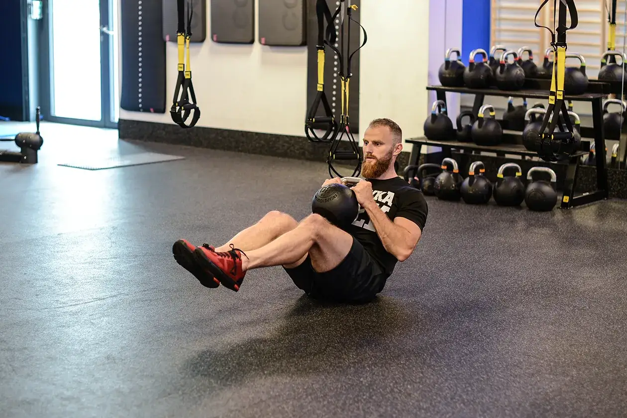 Mężczyzna wykonuje ćwiczenia na brzuch z kettlebell. Intensywny trening w siłowni.