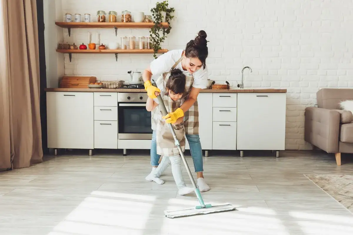 Madre e hija aprenden como limpiar tu casa juntas, pasando la mopa por el suelo de la cocina.