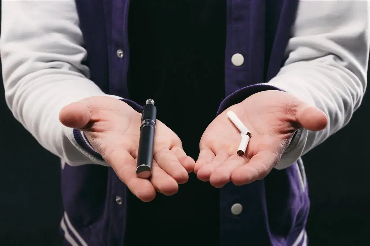 Manos abiertas: en una, un vaper; en la otra, un cigarro roto. La elección entre dos hábitos.