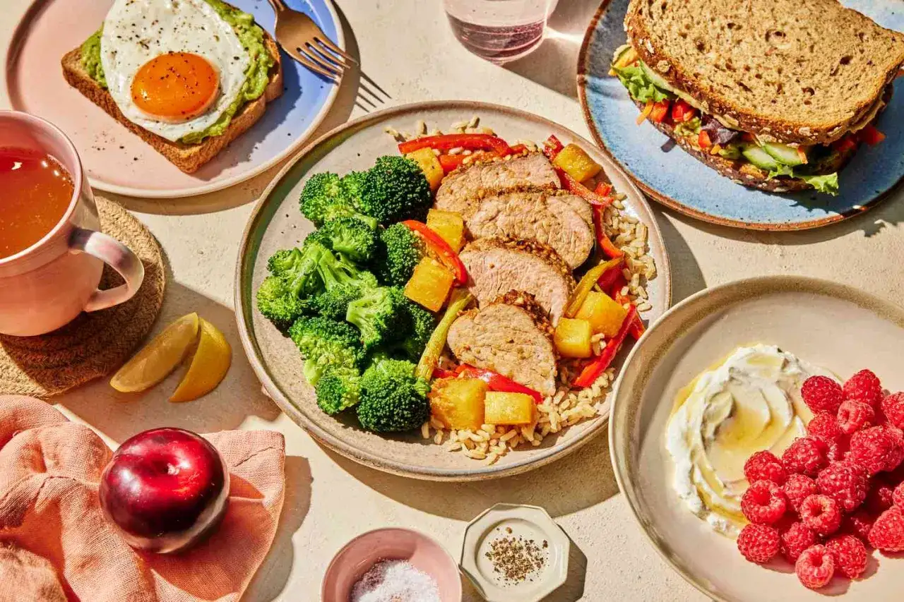 Zdrowe posiłki na talerzach: pieczony łosoś z brokułami, kanapka z awokado i jajkiem, deser z malinami. Idealne na dietę 1000 kcal.