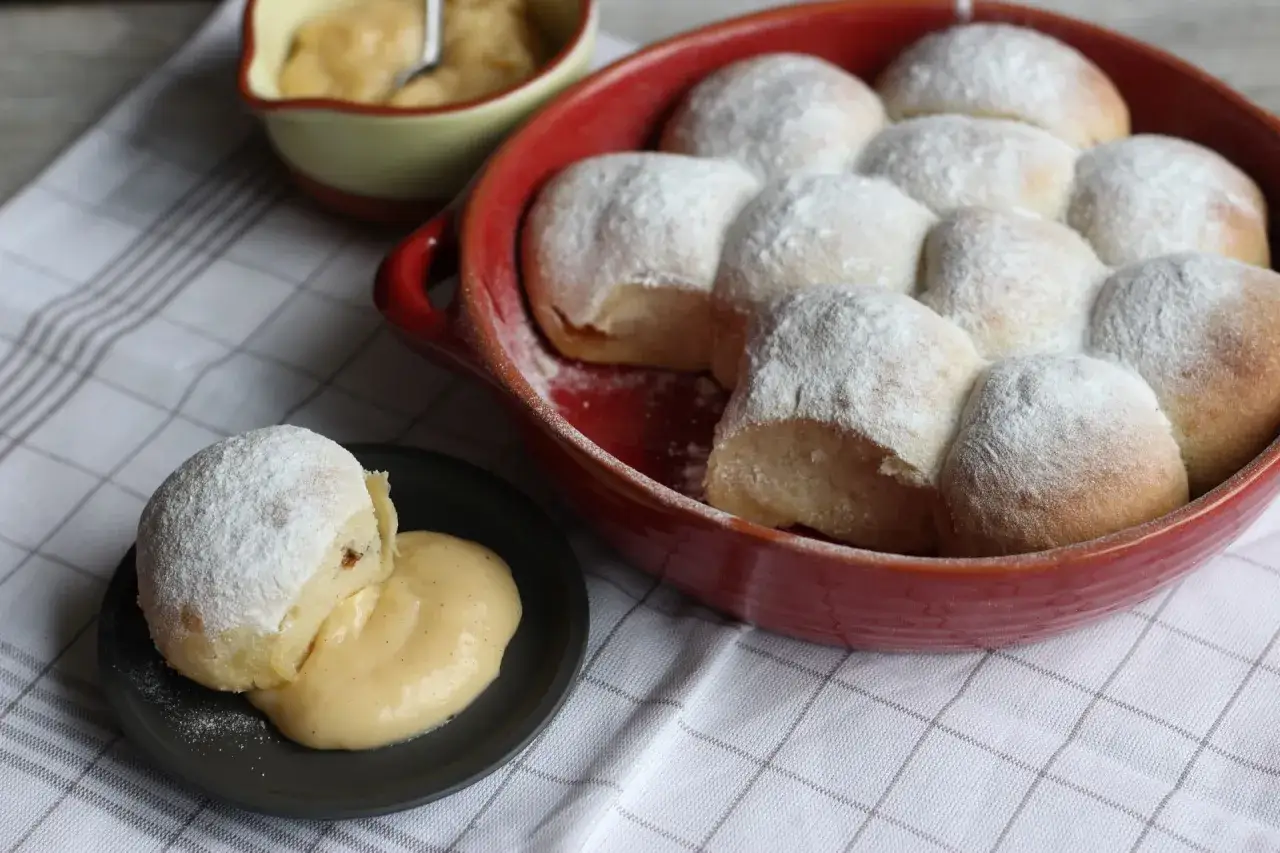 Frisch gebackene Buchteln mit Puderzucker bestreut, serviert mit Vanillesauce. Ein köstliches Rezept für Buchteln!