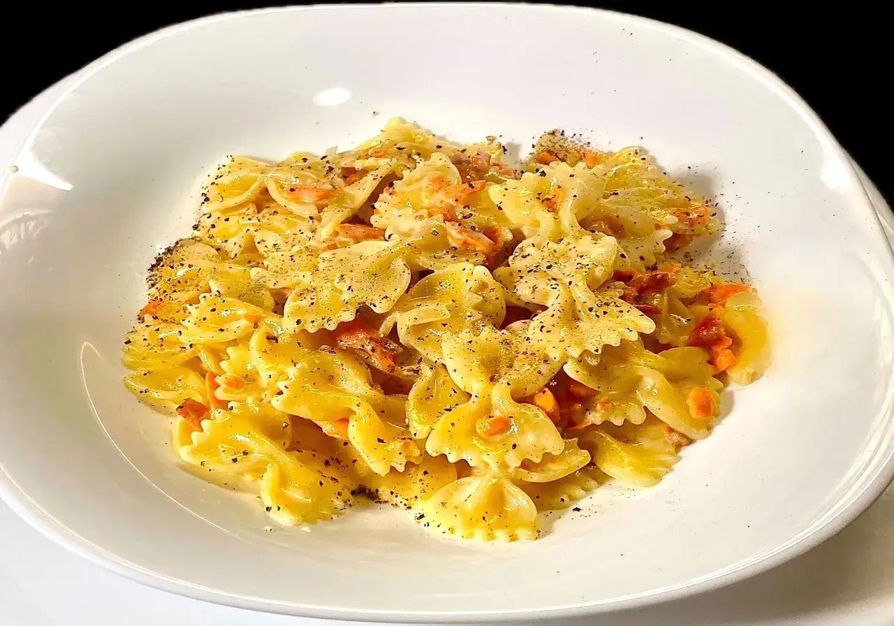 Farfalle al salmone cremose, condite con pepe nero macinato fresco, servite in un piatto bianco.