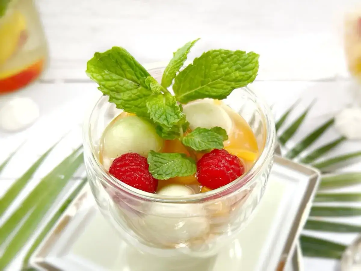 Délicieuse salade de fruits d'été : melon, pêche, framboises et menthe fraîche dans un verre.