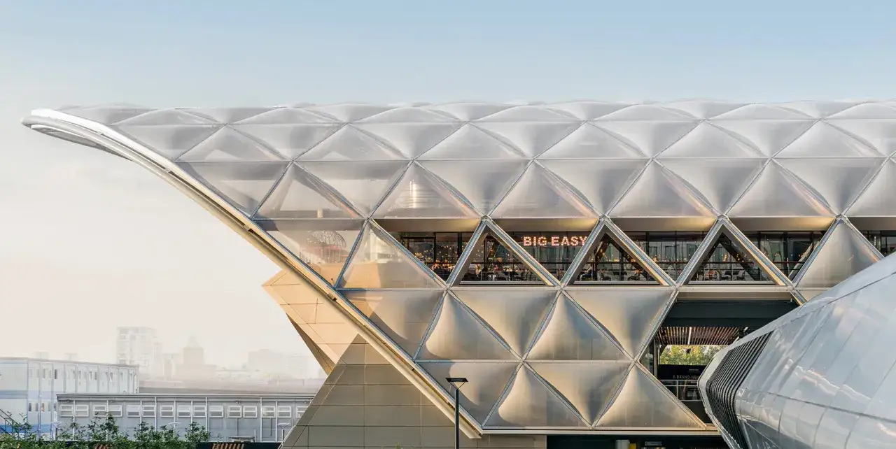 Nowoczesna fasada budynku z panelami etfe, tworząca geometryczny wzór. Wewnątrz widoczna restauracja 