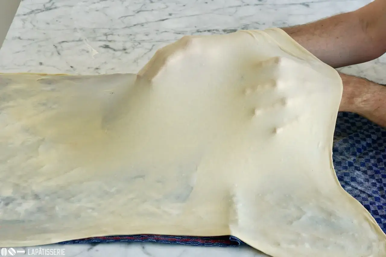 Hände dehnen den hauchdünnen Strudelteig für ein perfektes Strudelrezept.