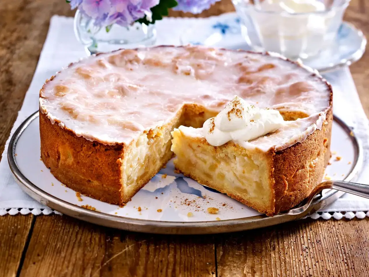Ein saftiger Apfelkuchen mit Zuckerguss und Sahnetupfer, bereit zum Servieren.