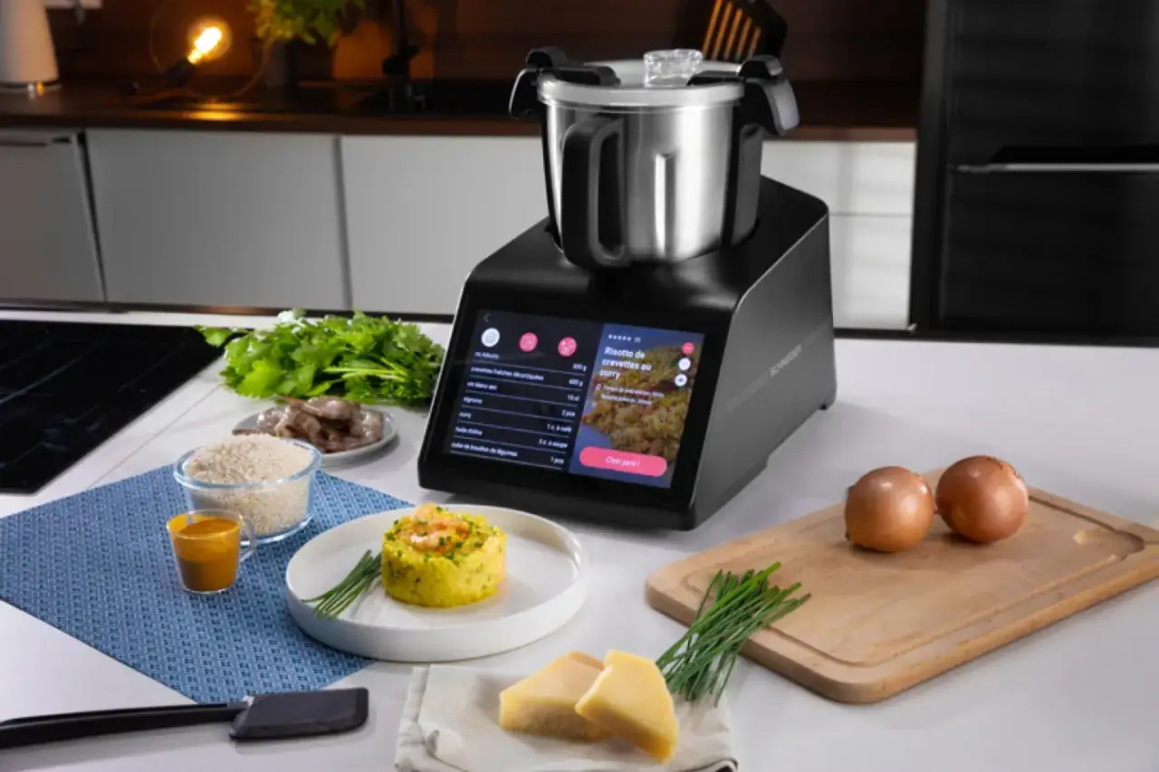 Robot cuiseur affichant une recette de risotto de crevettes au curry. Les ingrédients sont prêts : riz, crevettes, oignons, coriandre, fromage. Une aide précieuse pour votre recette Monsieur Cuisine.
