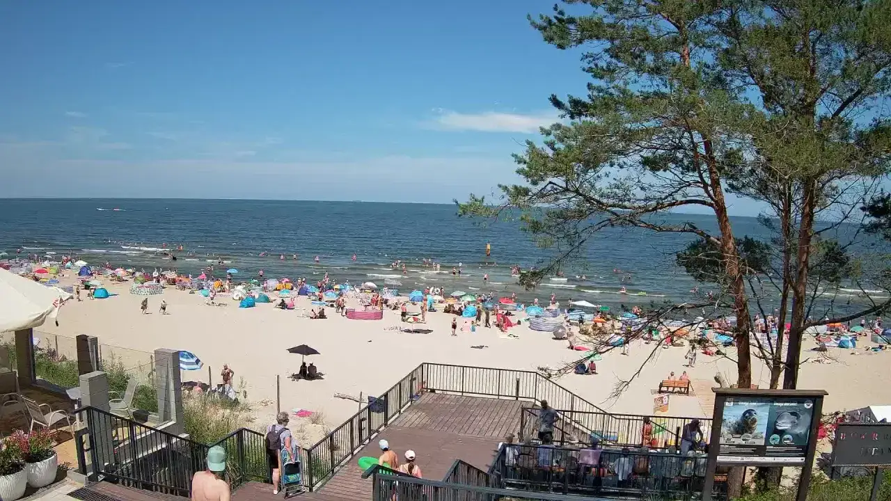 Słoneczna stegna plaża tętni życiem. Tłumy ludzi odpoczywają pod kolorowymi parasolami, kąpią się w morzu i spacerują po piasku.