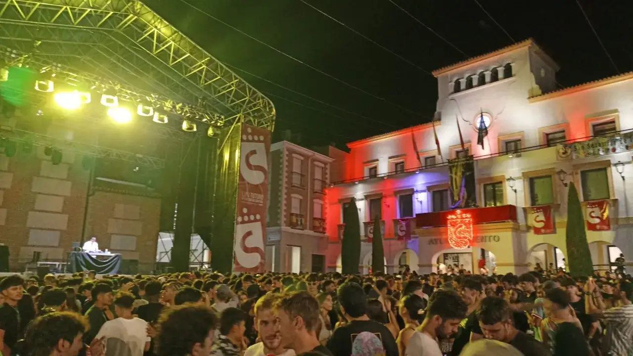 Multitud disfrutando de las fiestas San Sebastián de los Reyes, con un escenario iluminado y el ayuntamiento decorado.