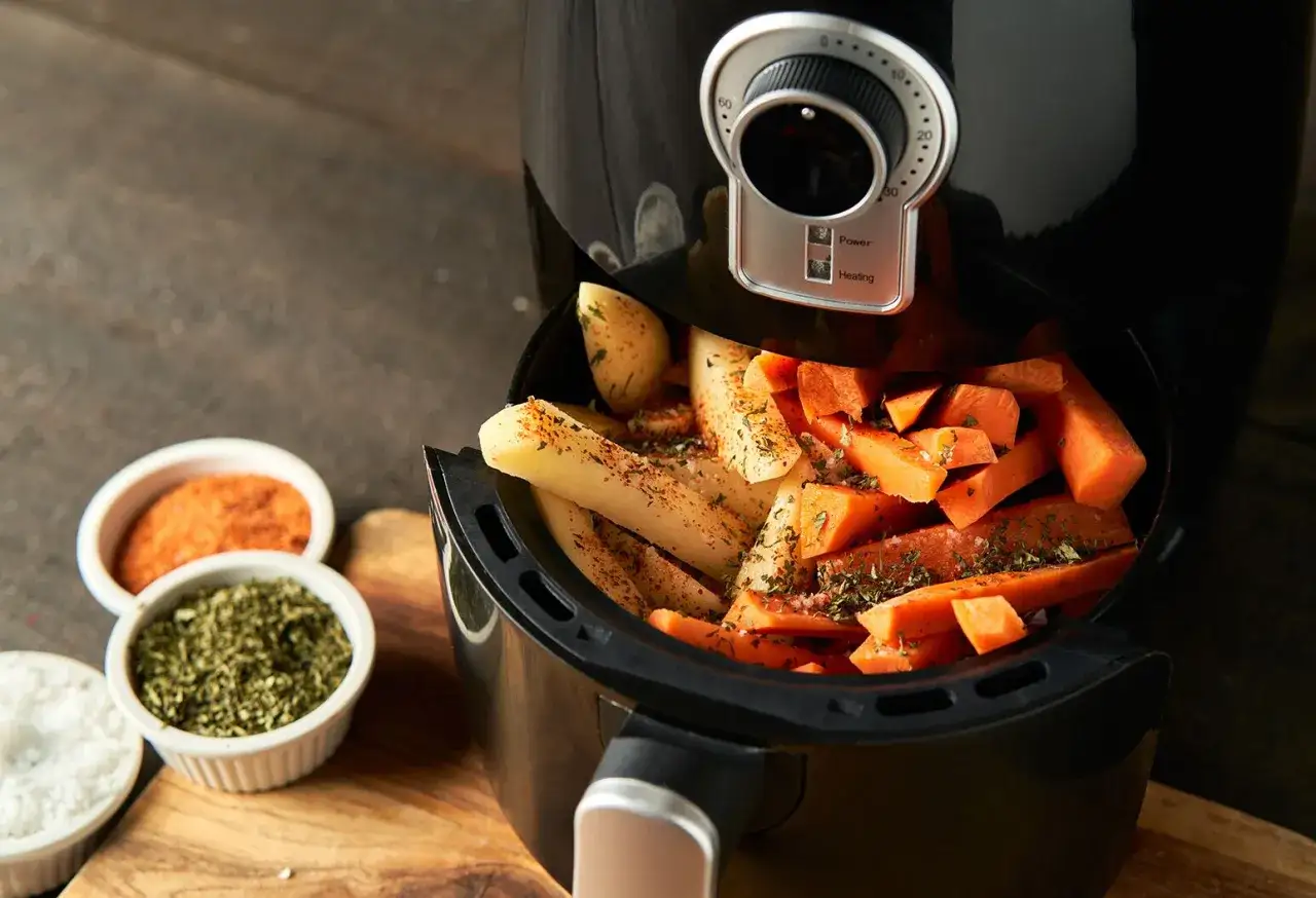 Zobacz, jak działa air fryer: ziemniaki i marchewka w koszu, gotowe do pieczenia. Obok przyprawy.