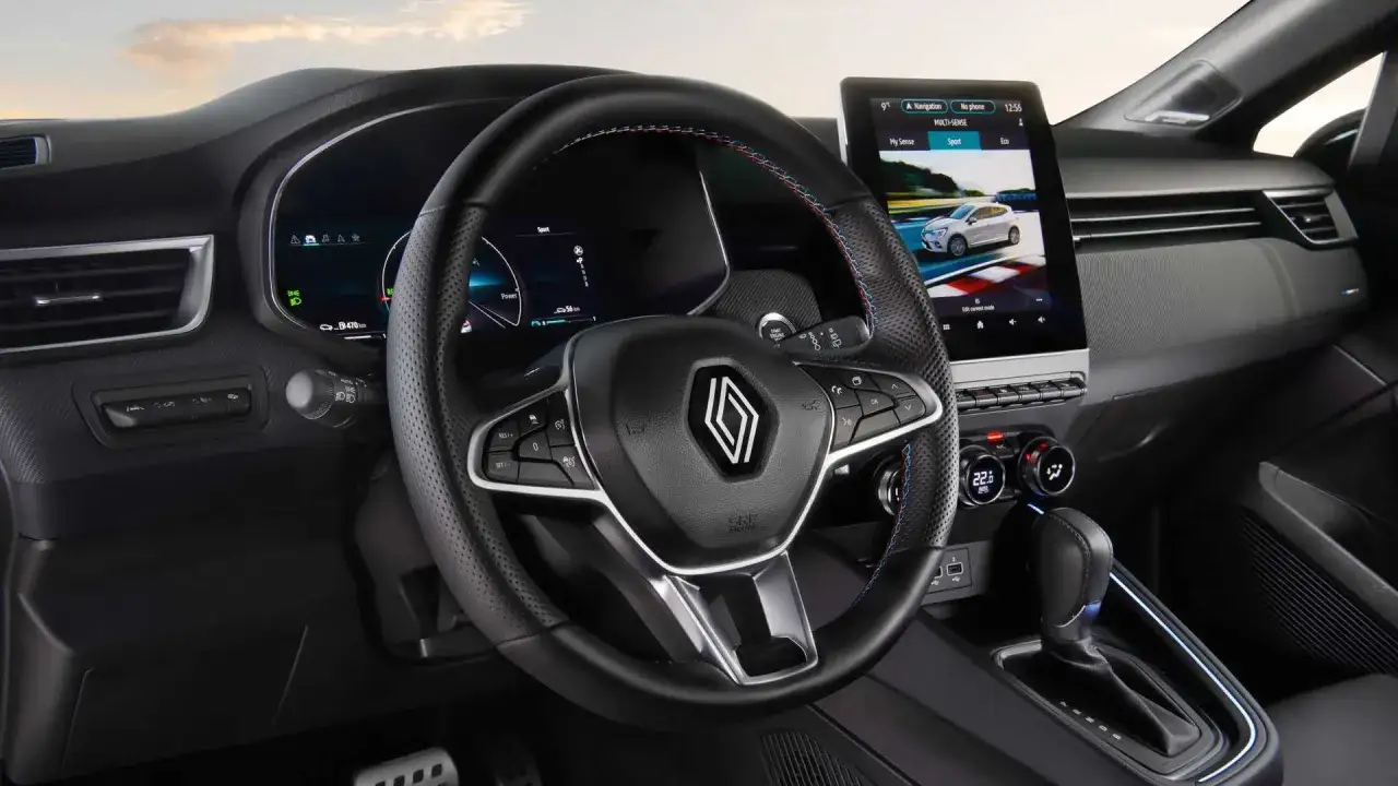 Wnętrze Renault Clio 2024 z nowoczesnym ekranem dotykowym i cyfrowymi zegarami. Kierownica z przeszyciami w kolorach francuskiej flagi.