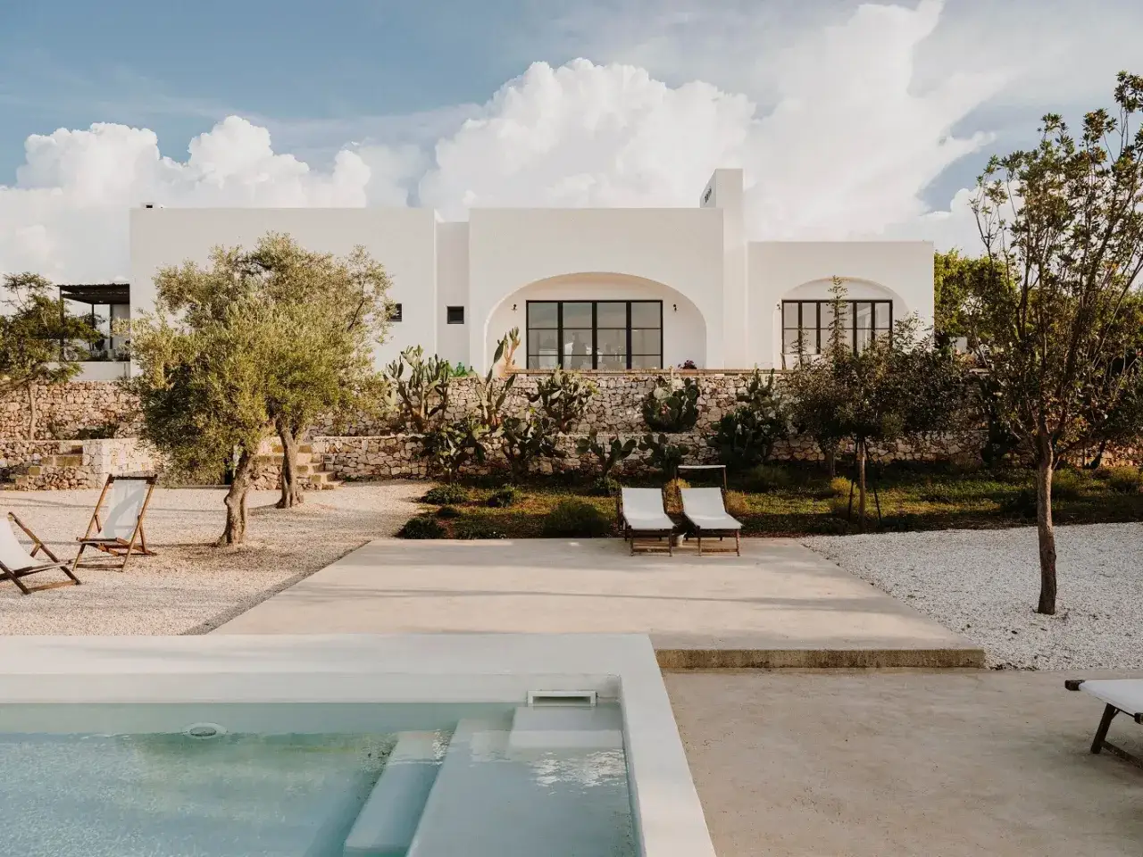 Masseria per bambini in Puglia: piscina, ulivi e cactus creano un'oasi di relax sotto il cielo azzurro.