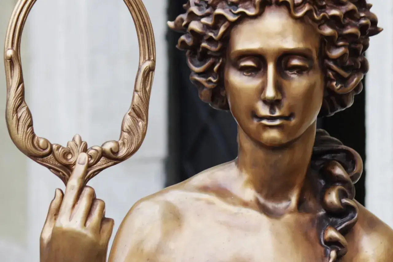 Statue en bronze d'une d&eacute;esse de la beaut&eacute; tenant un miroir orn&eacute;. Ses cheveux boucl&eacute;s encadrent un visage serein.