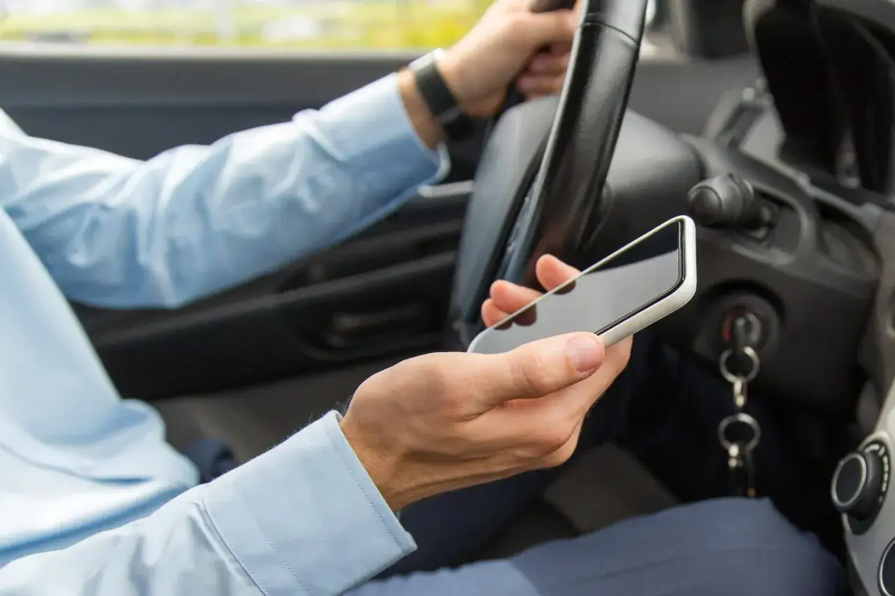Conducteur tenant un téléphone au volant, ignorant la nouvelle loi. Danger sur la route.