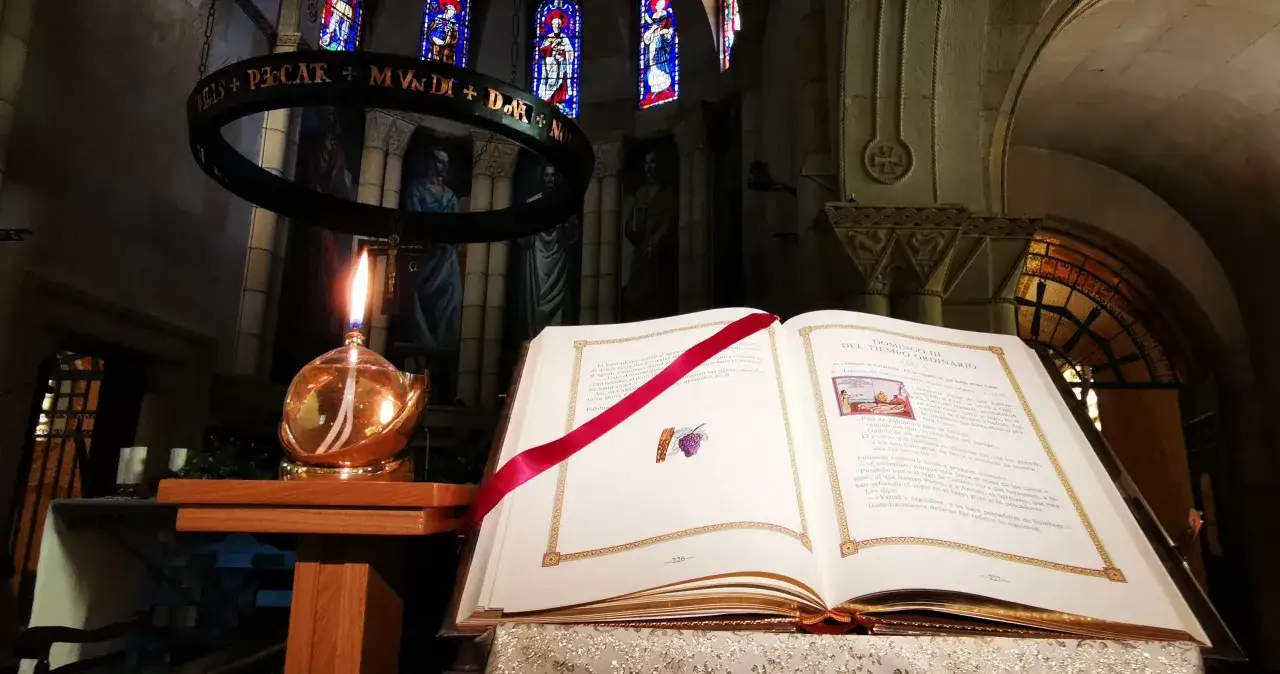 W kościele płonie świeca, obok otwarta księga z tekstem na czytanie i psalm na dziś.