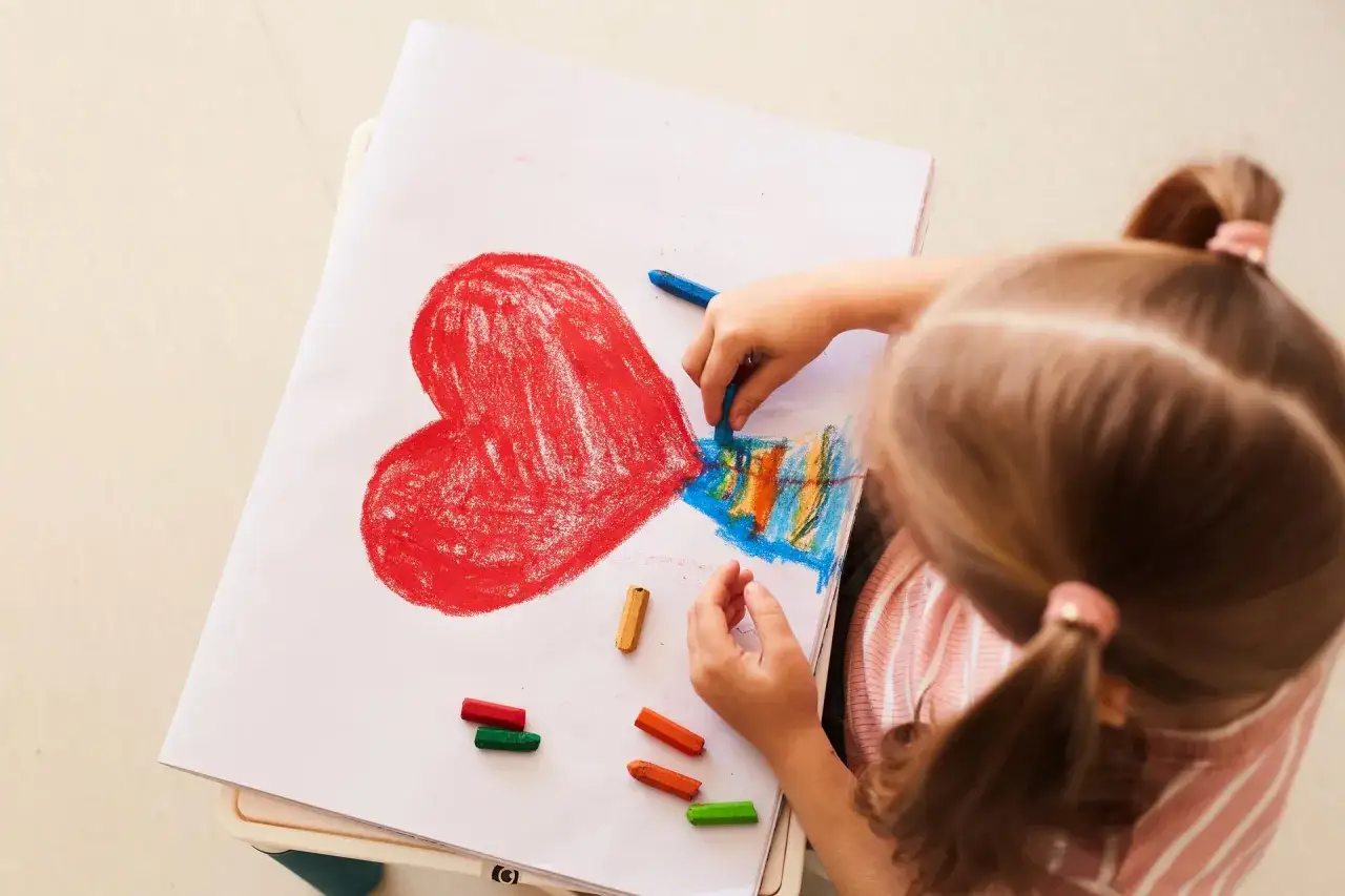 Dziecko rysuje kredkami serce i kolorowe paski. Czy to zagadka o mamie?