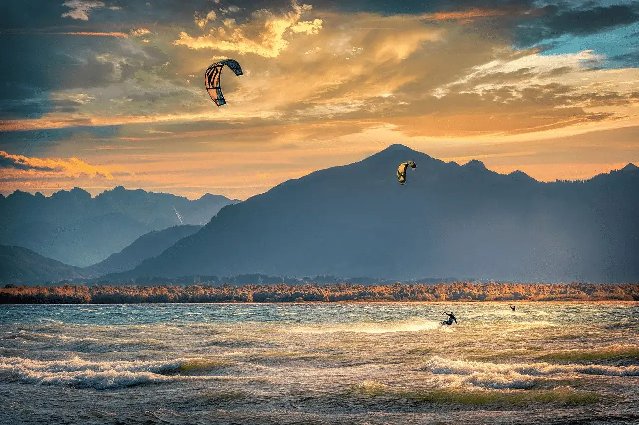 Kitesurfer genießen das Windsurfen am Chiemsee bei Sonnenuntergang. Berge im Hintergrund, dramatische Wolken.