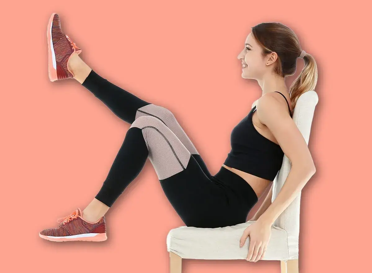 Femme souriante faisant un exercice pour comment muscler ses cuisses après 60 ans, assise sur une chaise, jambe levée.