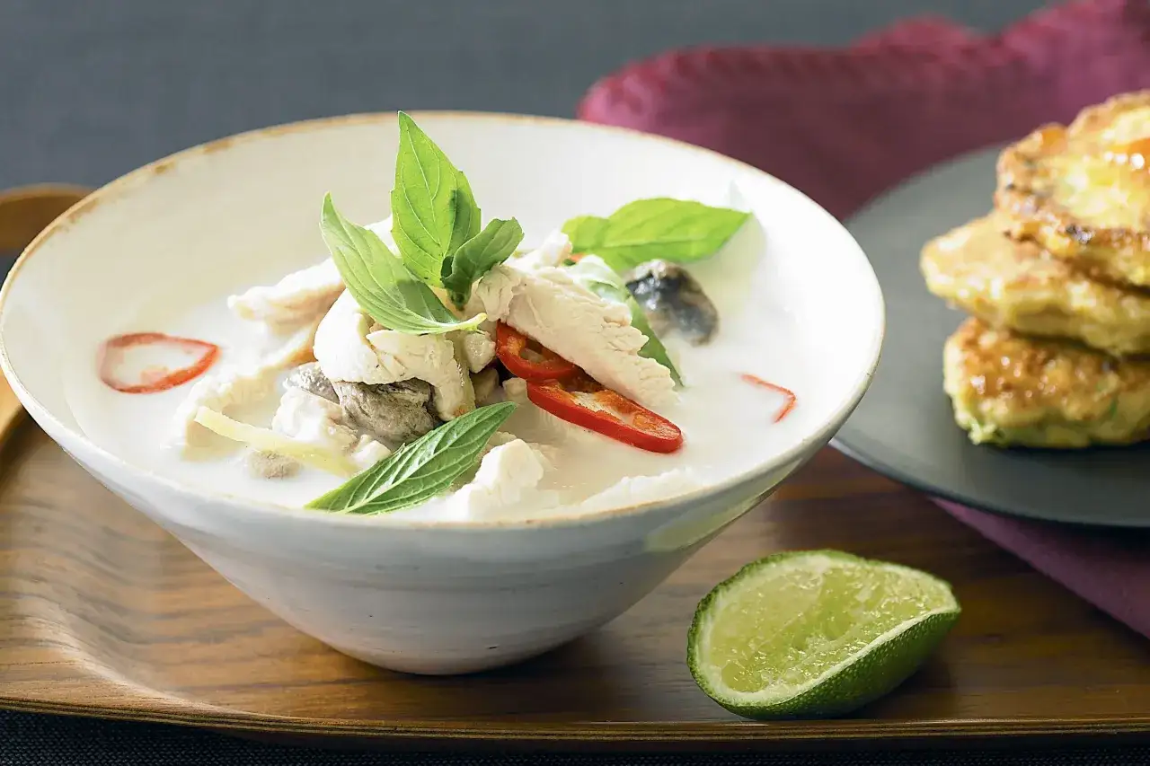 En sk&aring;l med kr&auml;mig tom kha gai med kyckling, svamp och f&auml;rska &ouml;rter. En limeklyfta ligger bredvid.