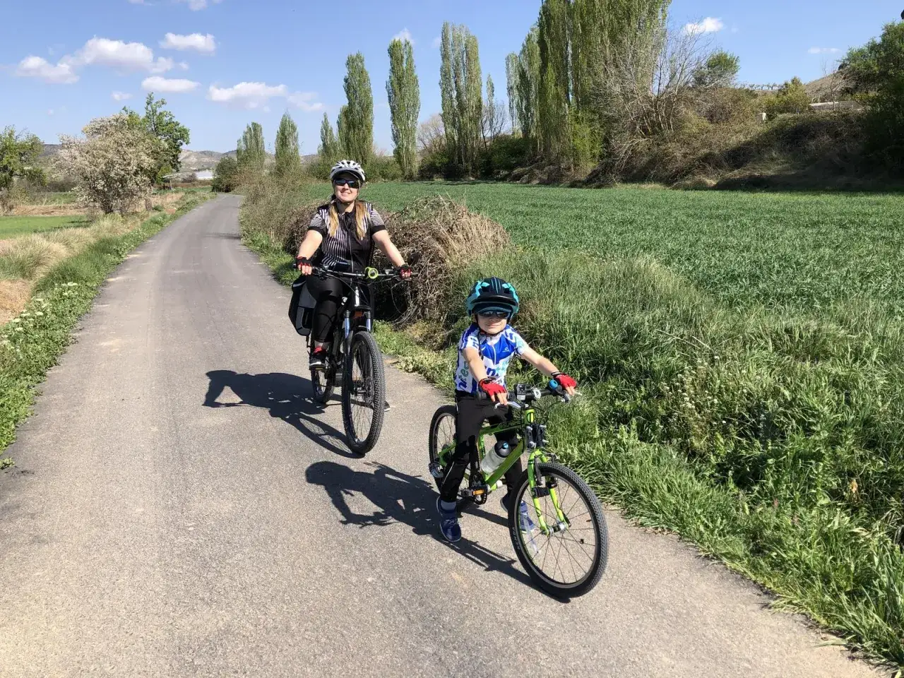 Madre e hijo disfrutan de un paseo en bicicleta por la vía verde del Tajuña, rodeados de campos verdes y árboles.