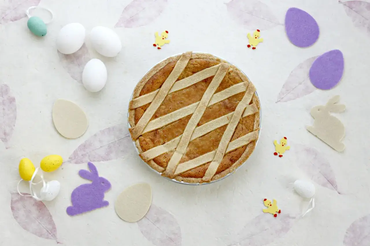 La pastiera è pronta per Pasqua, con tante strisce dorate che la rendono invitante. Uova, pulcini e coniglietti completano la scena.