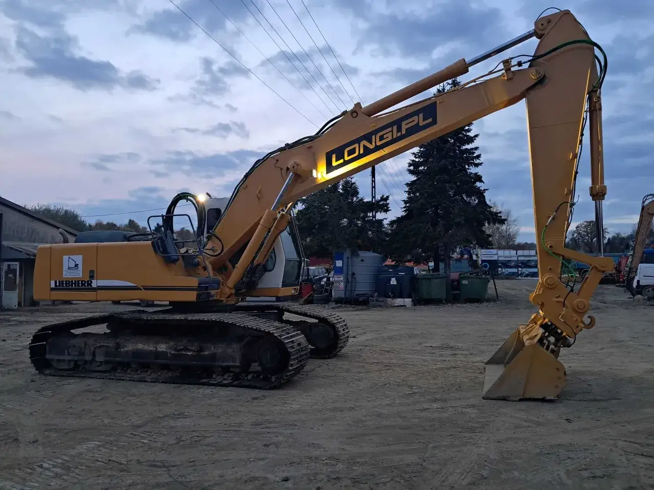 Żółta koparka gąsienicowa Liebherr z napisem LONG.PL gotowa do pracy. Dostępna do wynajęcia.
