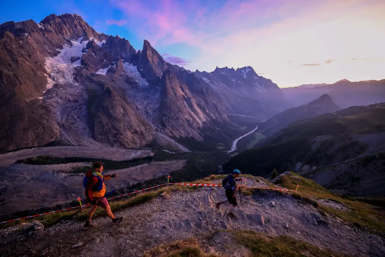 Biegacze na trasie ultra-trail du mont-blanc, wspinający się po skalistym zboczu na tle majestatycznych gór o zachodzie słońca.