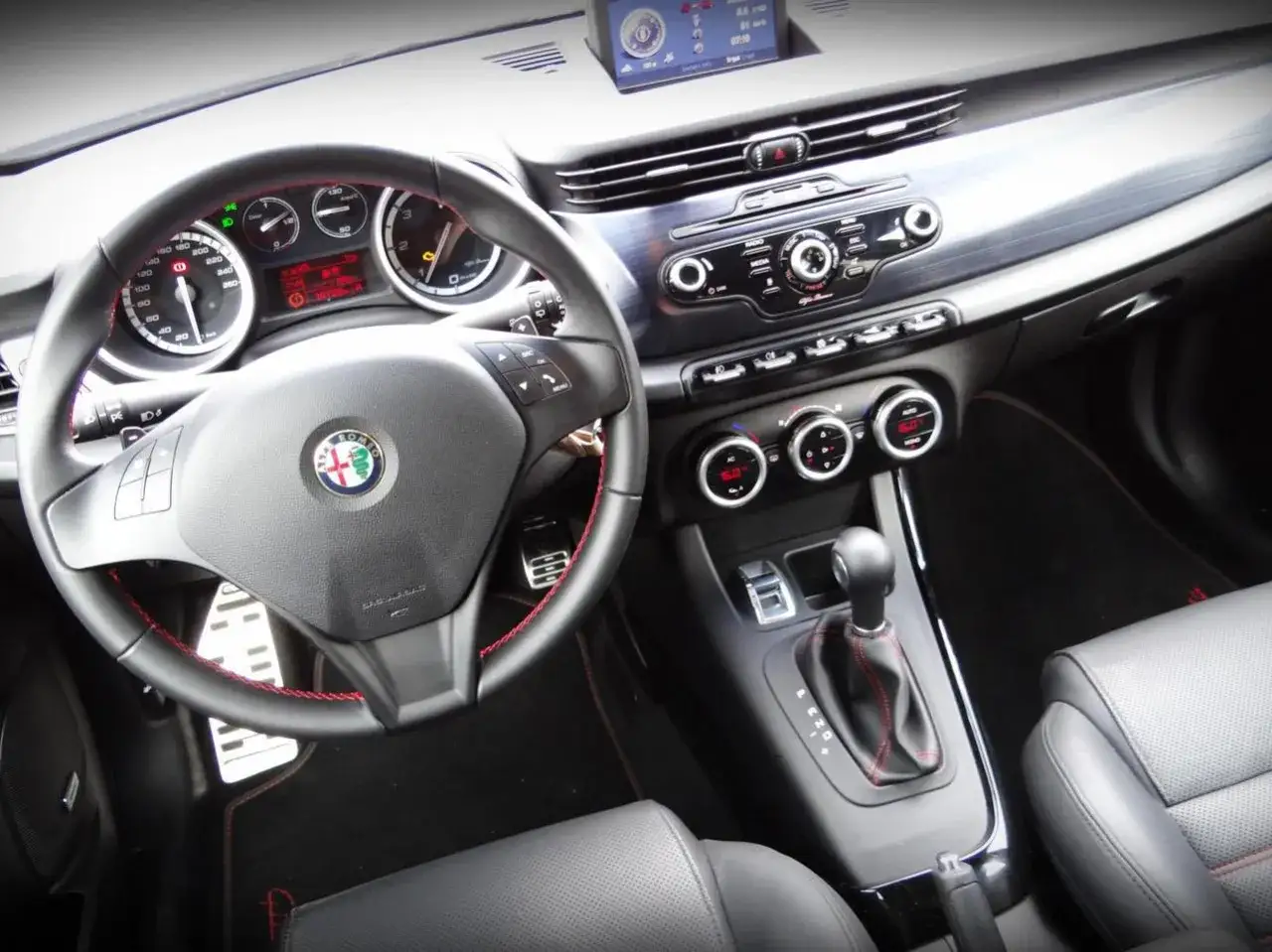 Wnętrze Alfa Romeo Giulietta. Kierownica, deska rozdzielcza i fotele. Wiele osób chwali ten model za styl i komfort, co potwierdzają liczne alfa romeo giulietta opinie.