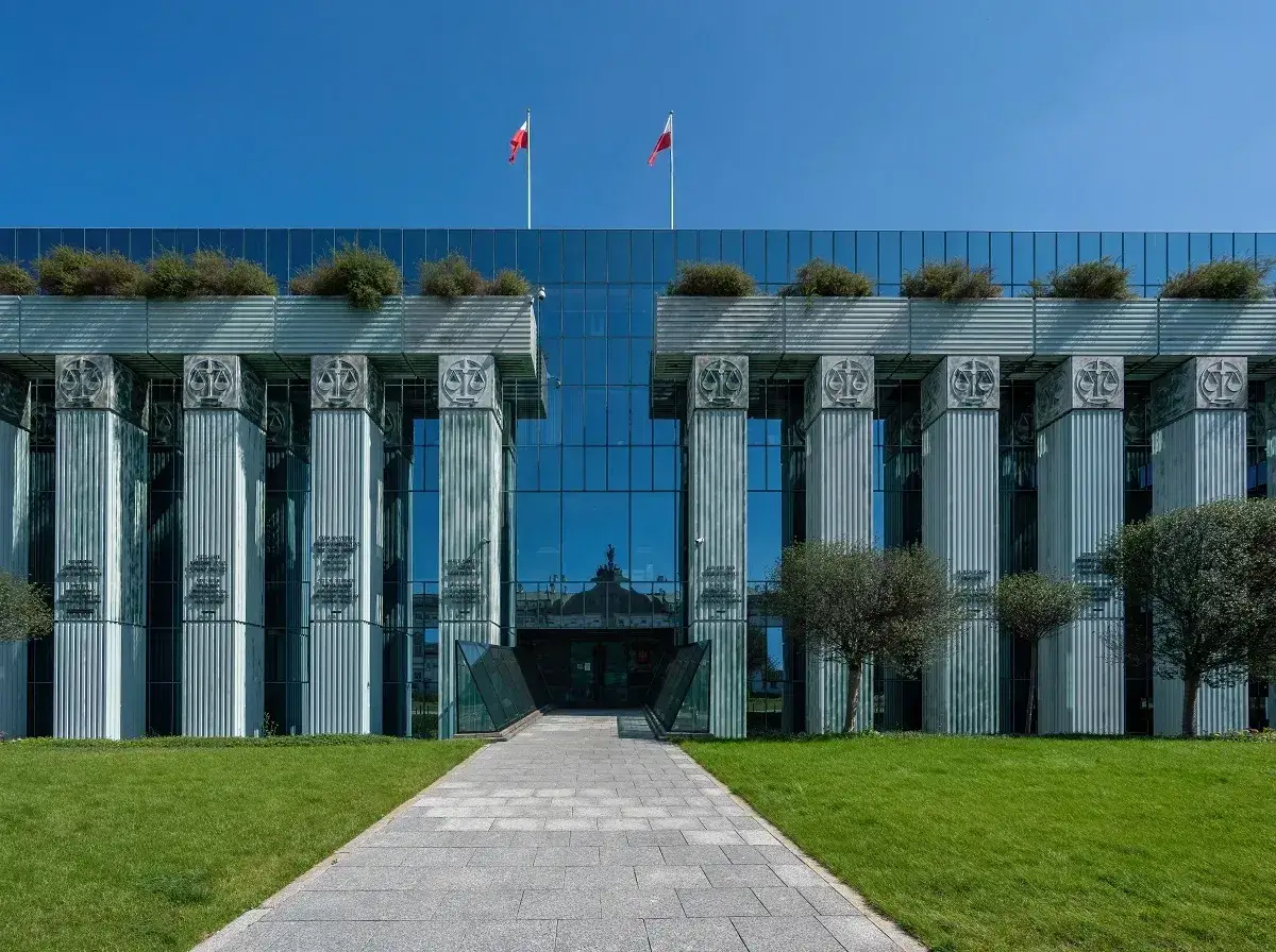 Nowoczesny budynek sądu z kolumnami i symbolami sprawiedliwości. Dwa polskie flagi powiewają na dachu. Jawne posiedzenie sądu odbywa się w tym miejscu.