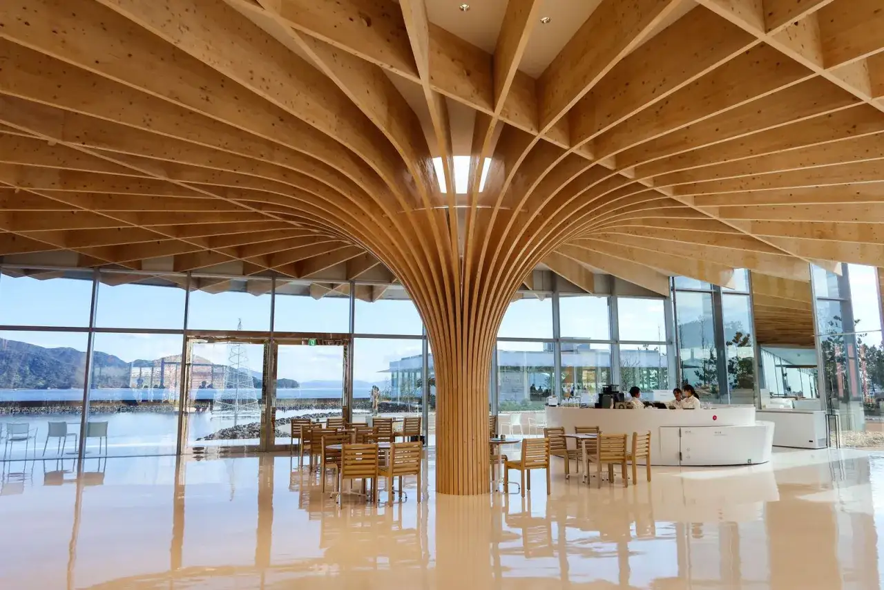 Interno moderno con soffitto in legno a forma di albero, tipico dell'architettura giapponese. Tavoli e sedie in legno, grandi vetrate con vista sul mare.
