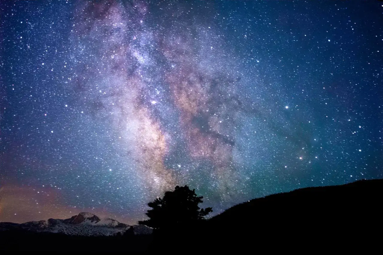 Via Lattea su montagne innevate e silhouette di alberi. Un cielo stellato che ispira a esplorare gli sbocchi lavorativi in astrofisica.