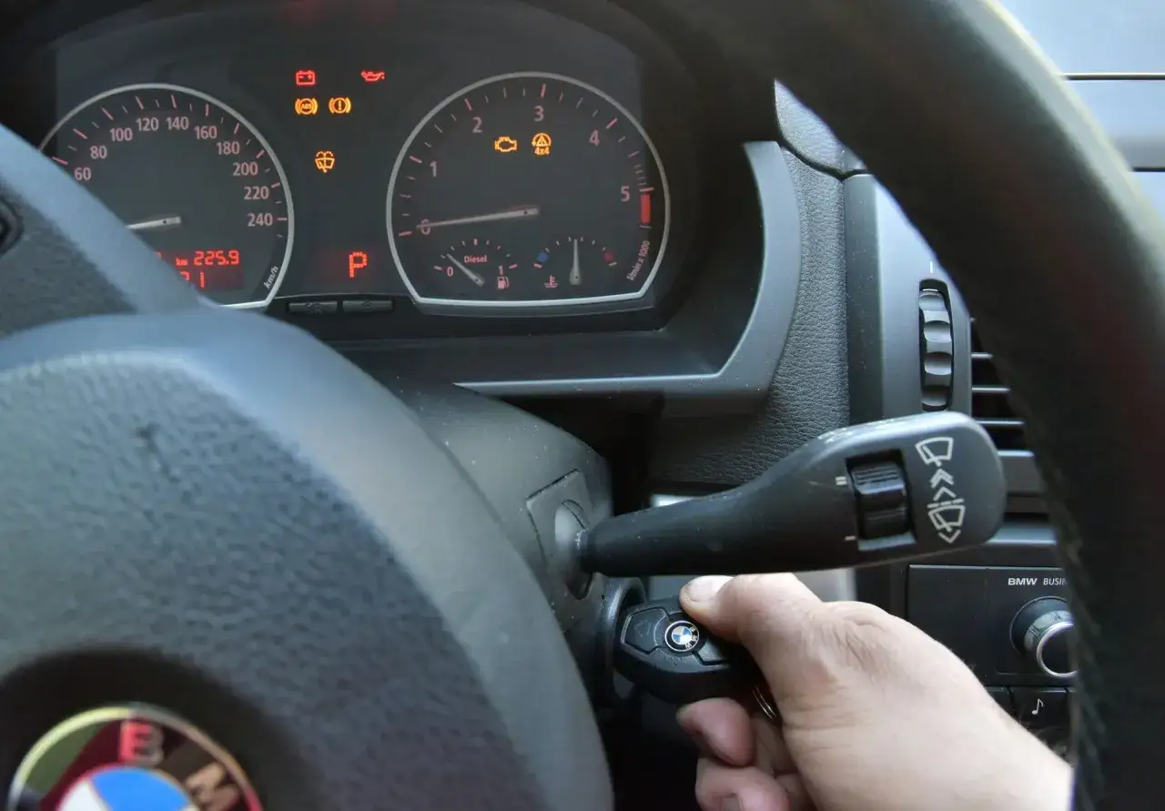 Ręka wkłada kluczyk do stacyjki. Na desce rozdzielczej świeci się kontrolka silnika, sugerując potrzebę dowiedzenia się, jak skasować błąd check engine bez komputera.