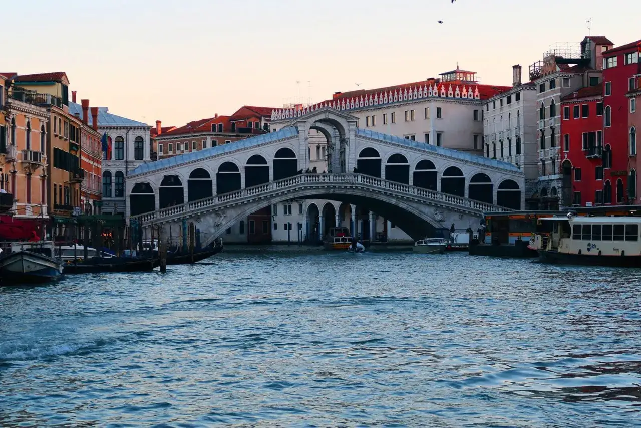 El puente de Rialto en Venecia, una vista icónica para tu plan de Venecia en 3 días. Barcos navegan por el canal.