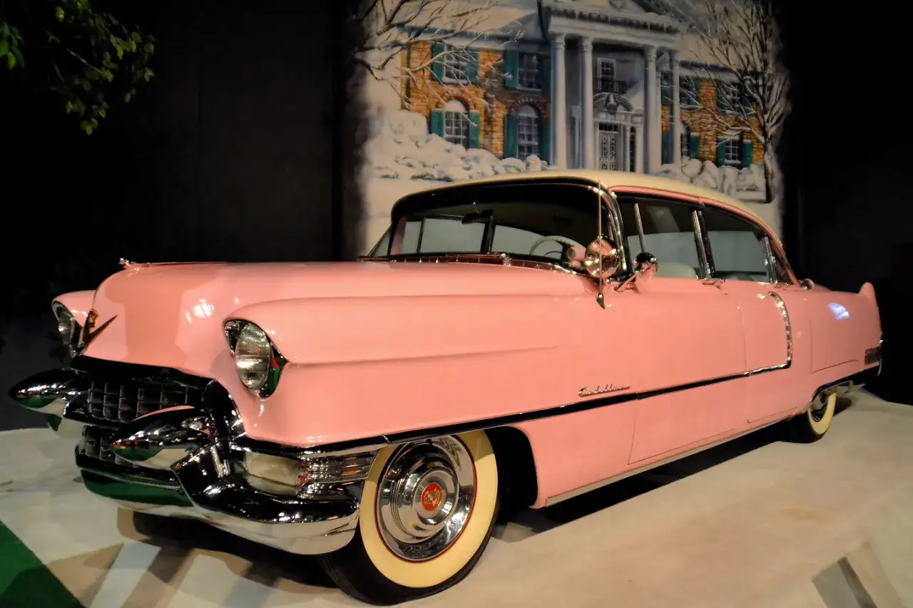 Ein rosafarbener Cadillac, wie ihn Elvis Presley liebte, steht vor einer gemalten Kulisse von Graceland.
