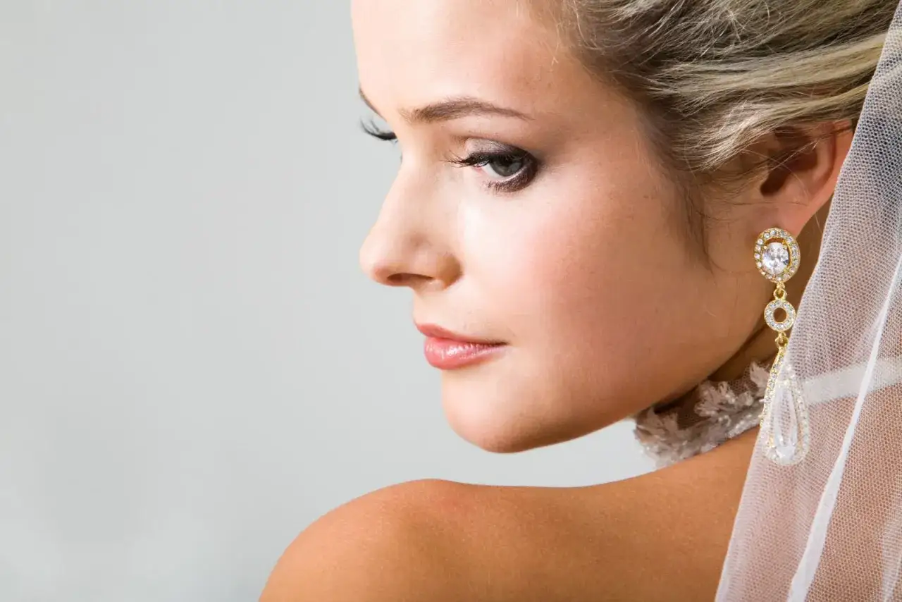 Primer plano de una novia con maquillajes de novia impecables, luciendo un pendiente de oro y diamantes.