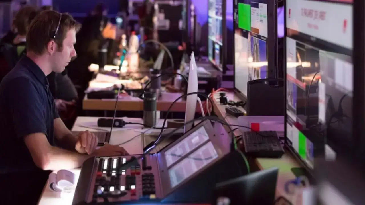 Mann mit Headset am Mischpult, &uuml;berwacht Monitore. Er arbeitet an einem Projekt, das unter den tvn tarifvertrag f&auml;llt.