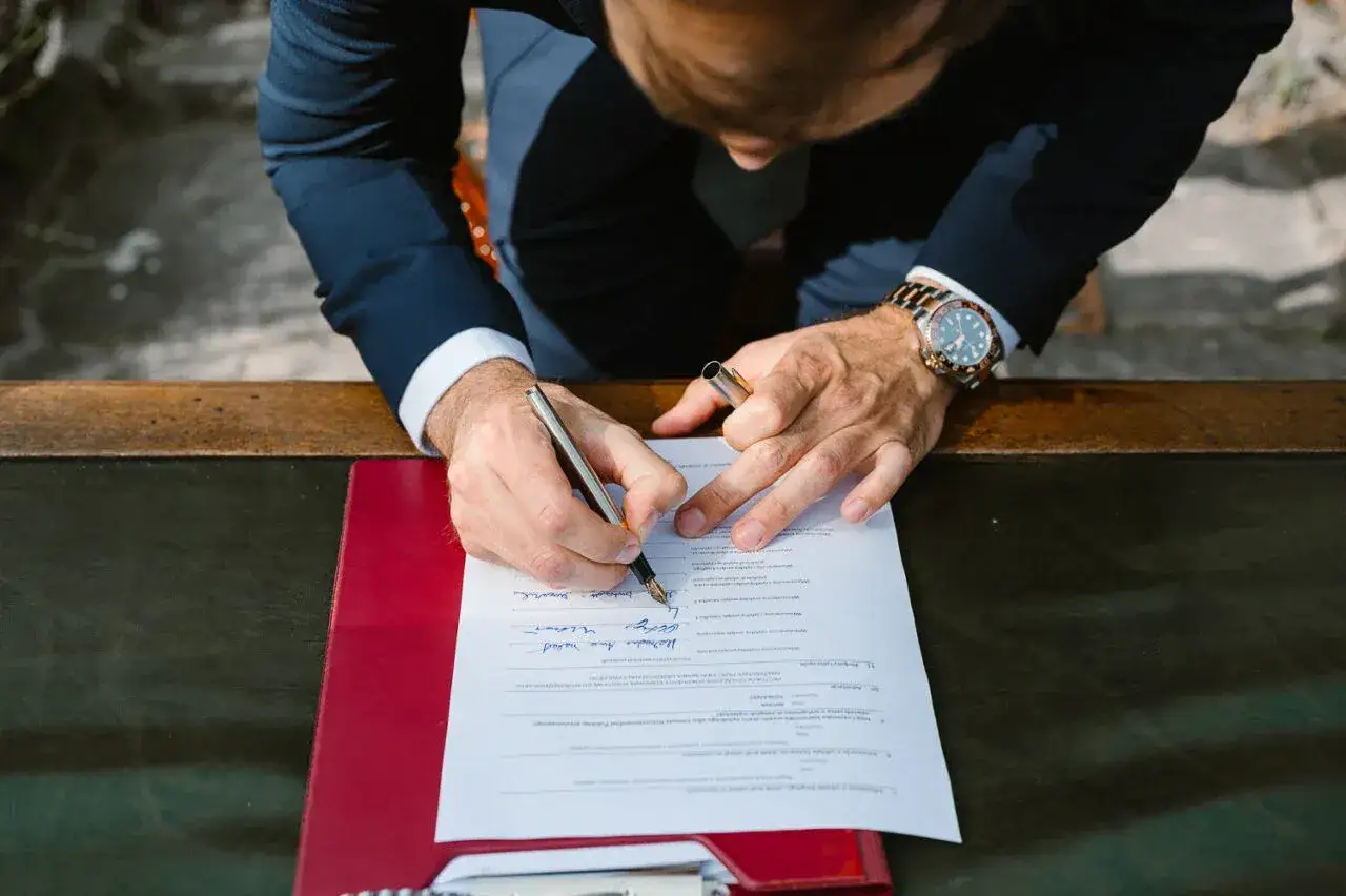 Mężczyzna w garniturze podpisuje dokument. Czy akt urodzenia jest potrzebny do ślubu? To pytanie może pojawić się podczas wypełniania formalności.
