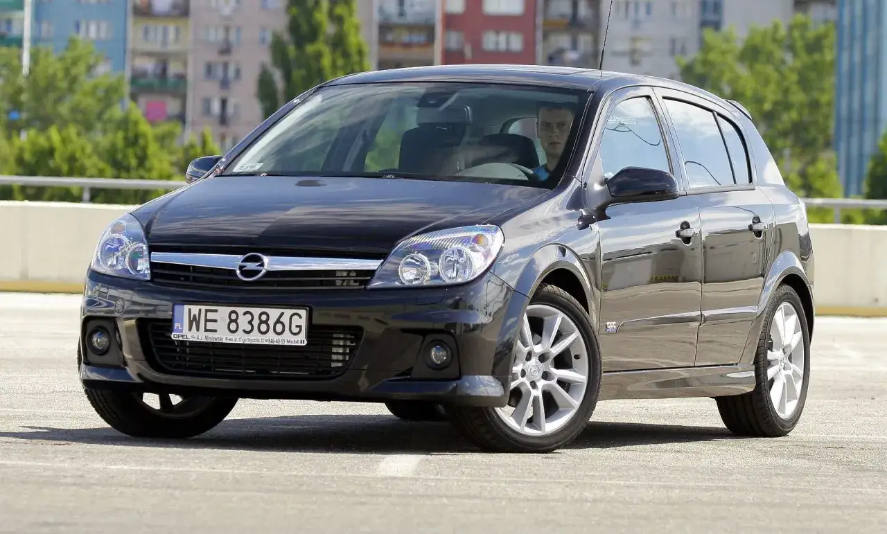 Czarny Opel Astra H z wyraźnymi przednimi światłami, w tym żarówkami.