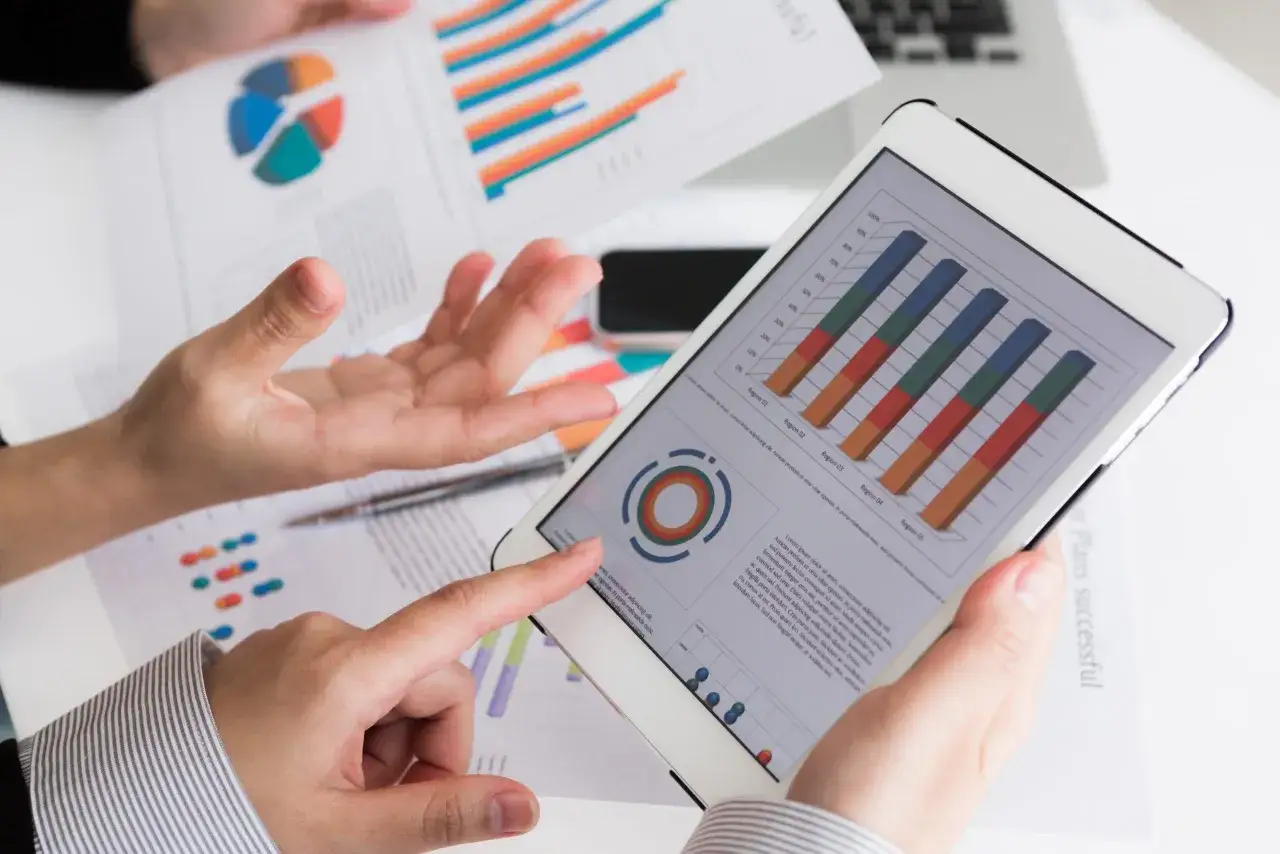 Manos analizan gráficos en tablet y papeles, revisando los requisitos para crear empresa online.