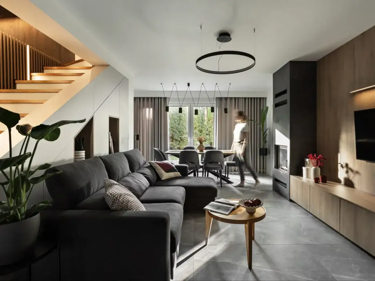 Nowoczesny salon z jadalnią, gdzie rozbudowa domu nadała przestrzeni nowy wymiar. Jasne schody, wygodna sofa i designerskie oświetlenie.