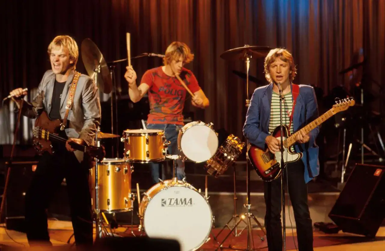 Le groupe Police en pleine performance, un trio iconique des années 80. Sting à la basse, Stewart Copeland à la batterie et Andy Summers à la guitare.