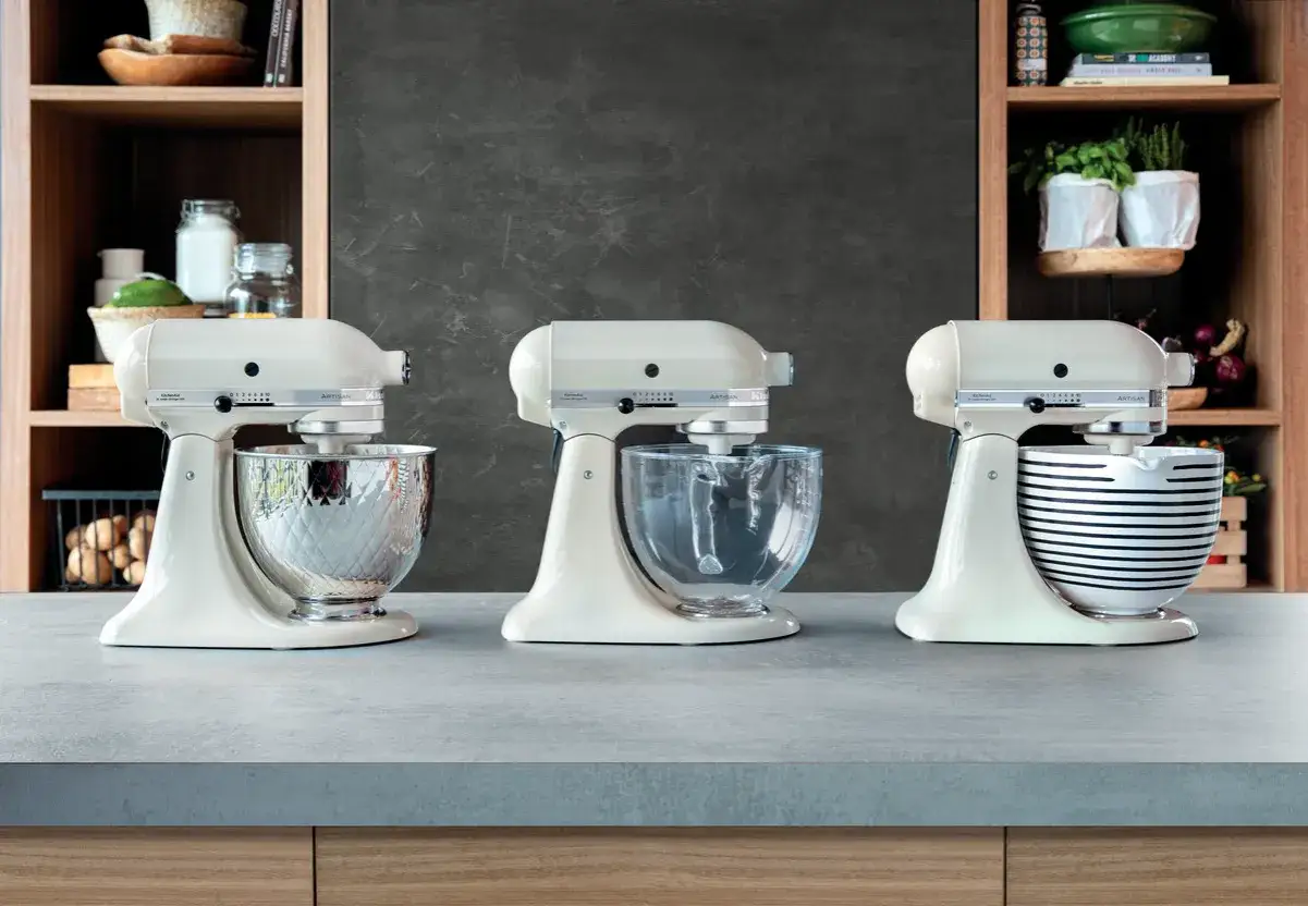 Trzy kremowe roboty planetarne KitchenAid Artisan, każdy z inną misą: metalową, szklaną i w paski. To najlepszy robot planetarny dla każdego kucharza.