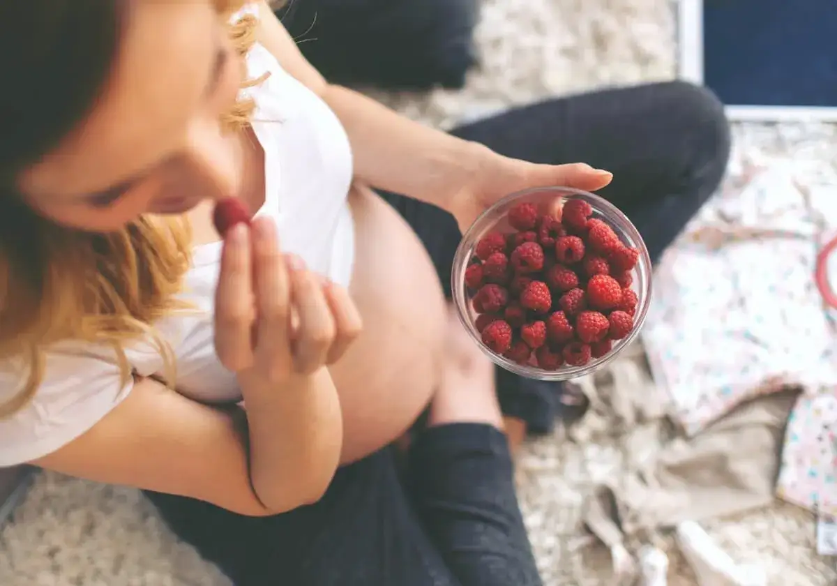 Gravid kvinna äter hallon från en skål. Hon verkar njuta av sin råbiff-liknande frukost.