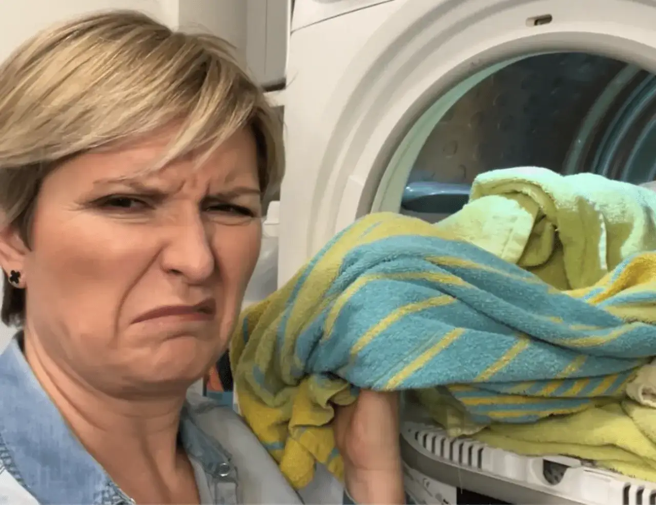 Kobieta z grymasem na twarzy czuje brzydki zapach z pralki, gdzie leżą mokre ręczniki.