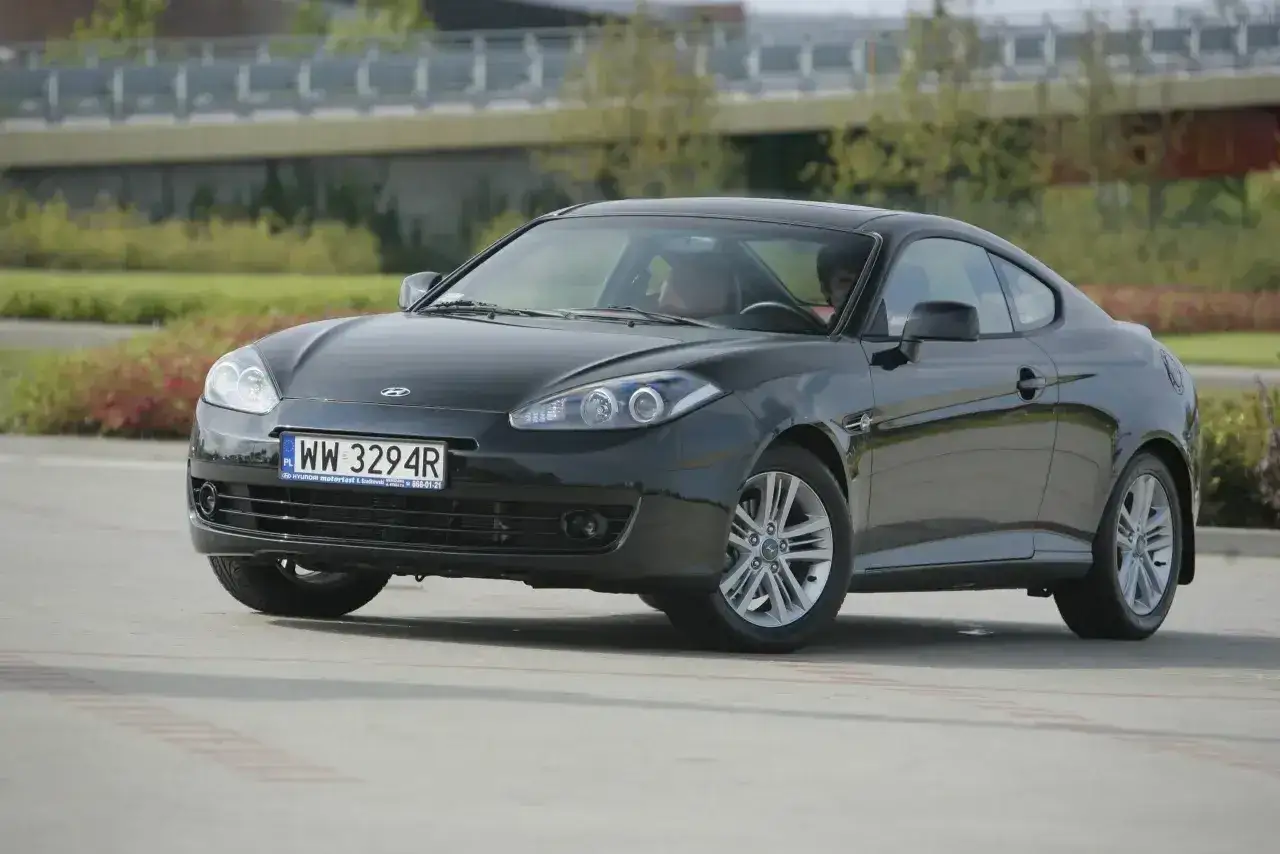 Czarny Hyundai Coupe 2.7 V6 z polskimi tablicami rejestracyjnymi WW 3294R zaparkowany na zewnątrz.