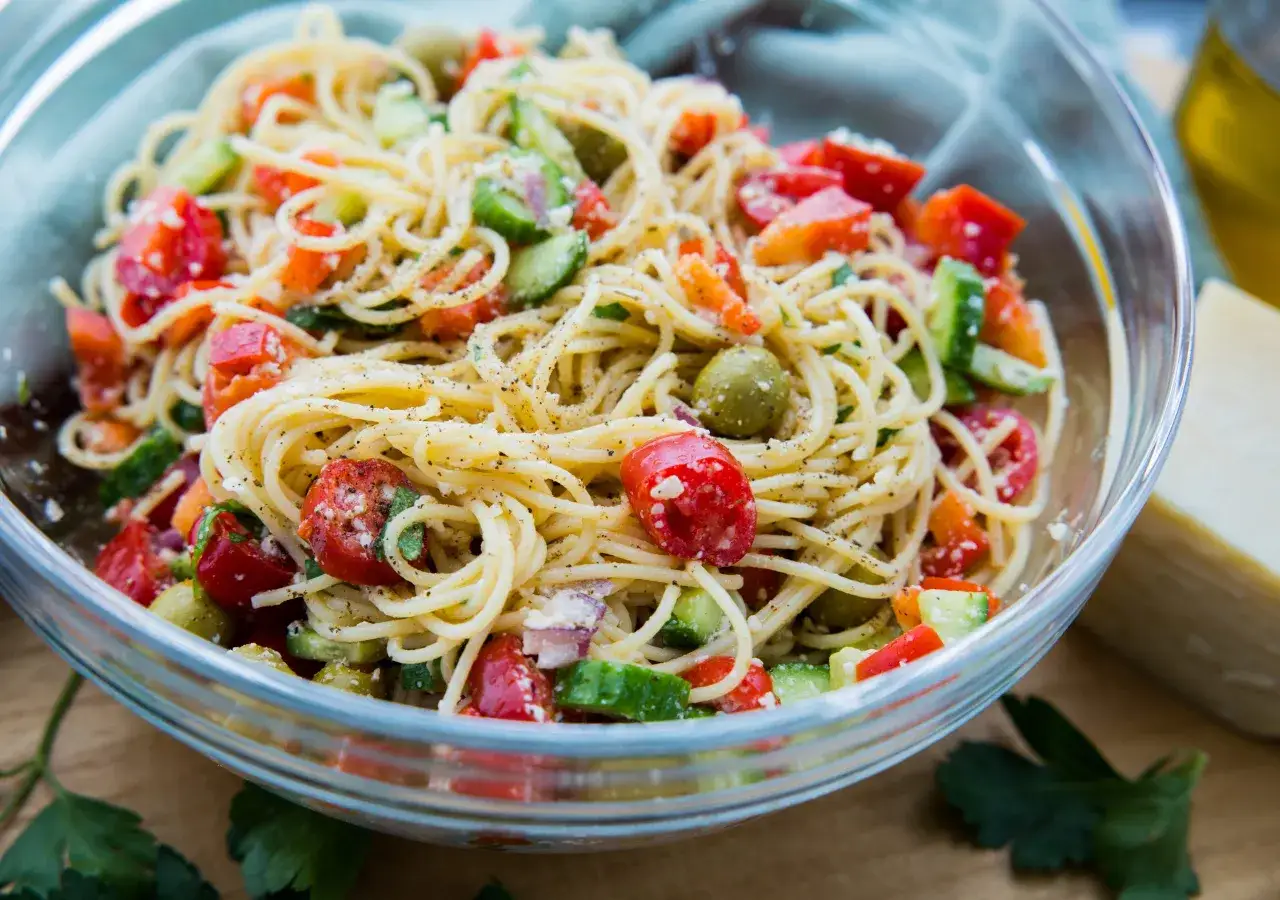 Frischer Spaghettisalat mit Knoblauch und Parmesan, garniert mit Tomaten, Gurken und Oliven.